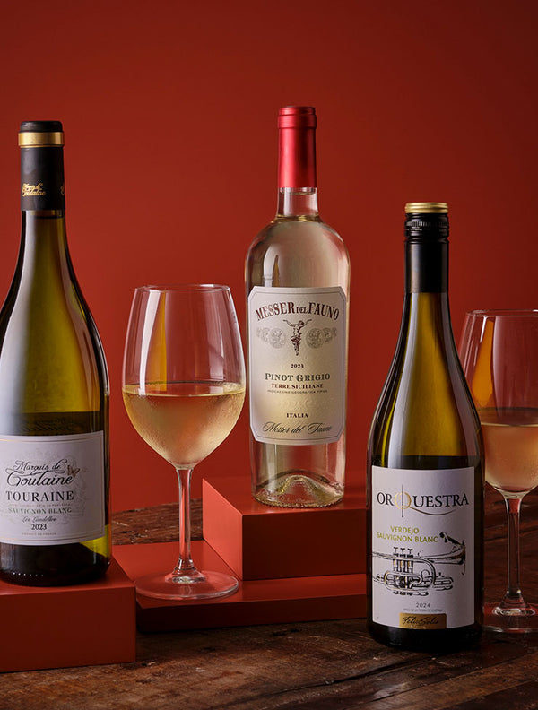Three bottles of white wine with elegant wine glasses on a rustic wooden table