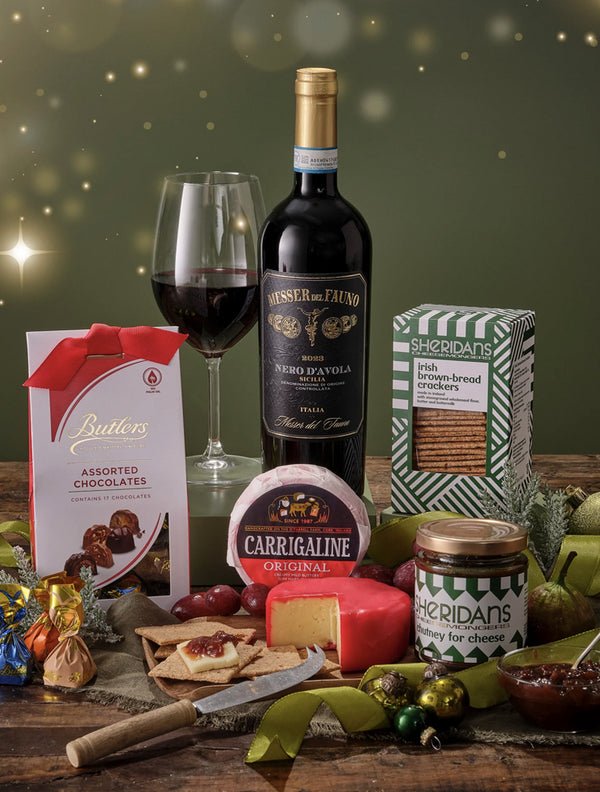 Gourmet gift set with wine, cheese, and snacks on a wooden table.