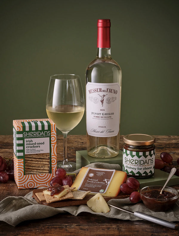 Wine bottle, glass, crackers, cheese, and grapes on a wooden table with a green background