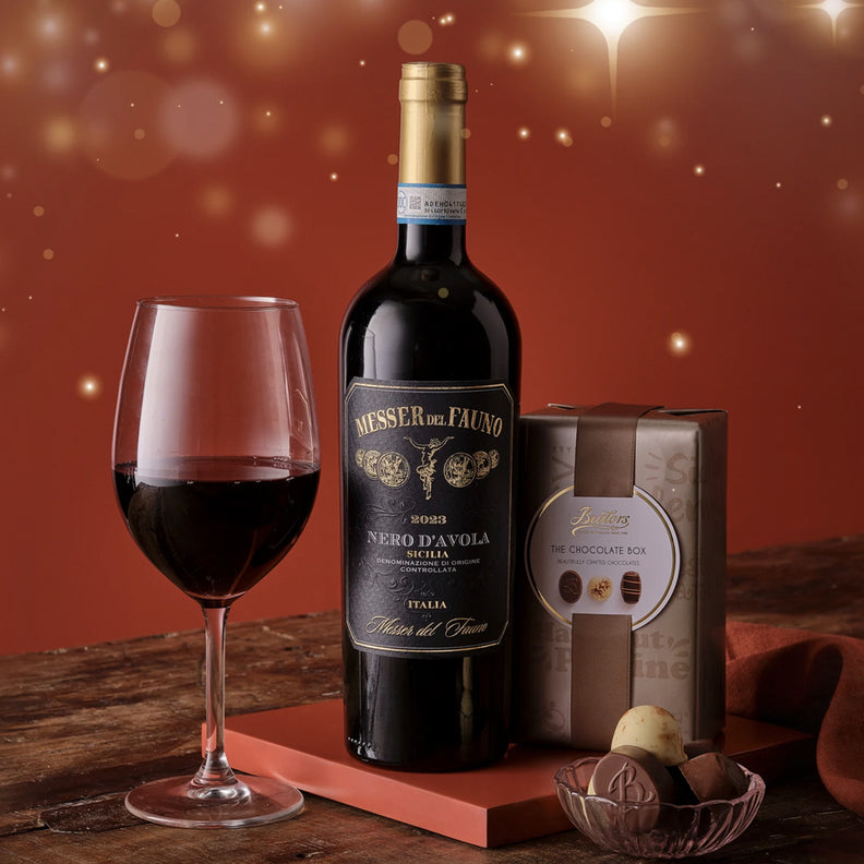 Bottle of red wine with a glass and gift box on a wooden surface with a warm, blurred background.