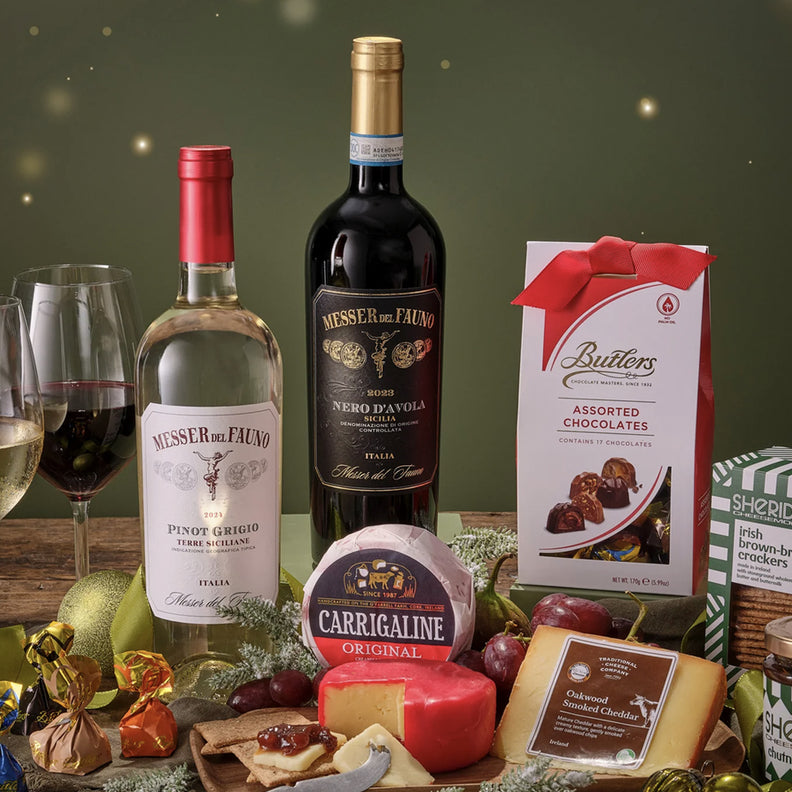 Wine bottles, glasses, and assorted cheeses on a wooden table with a dark green background.