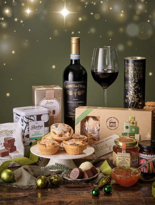 Gourmet gift set with wine, pies, and other treats on a wooden table.