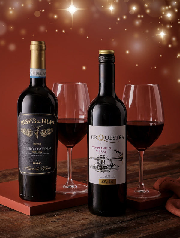 Two bottles of red wine with glasses on a wooden surface against a warm, glowing background.
