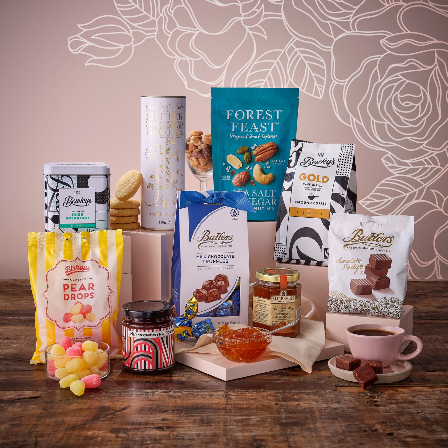 A Taste of Mum’s Kitchen Hamper arranged with wine biscuits chocolates and snacks on a pink backdrop