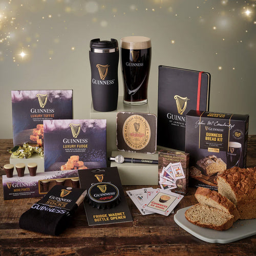 Collection of Guinness-themed products including a mug, notebook, fudge, and bread kit on a wooden table.