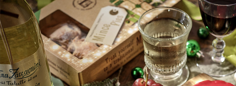 Wine bottle, glass of white wine, and gift box on a table with decorative elements.
