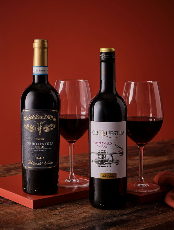 Pair of red wine bottles with elegant wine glasses on a rustic wooden table