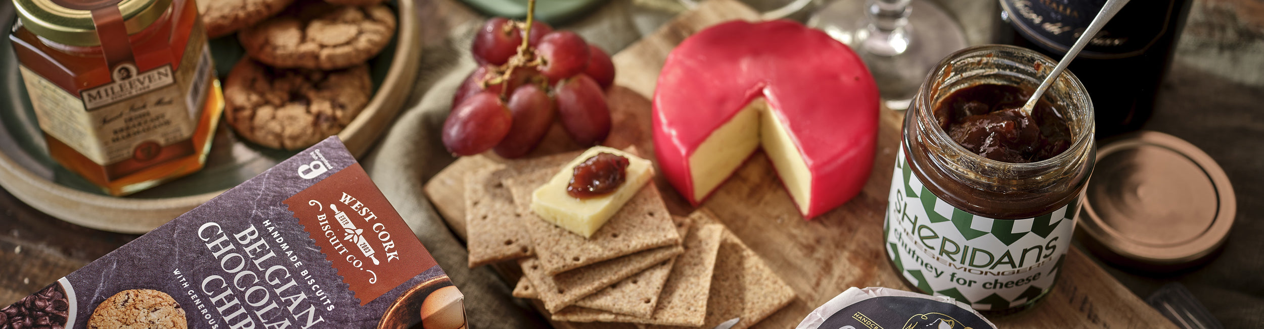 Assorted cheeses, crackers, and honey on a wooden board with a jar of chutney.