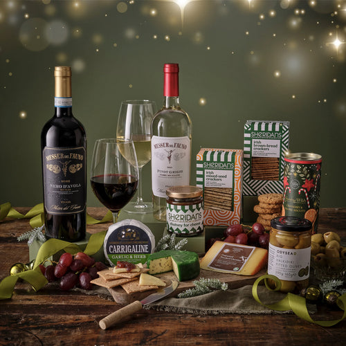 Wine bottles, glasses, and assorted snacks on a wooden table with a festive background.
