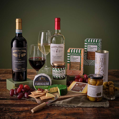 Gourmet gift set with wine, cheese, and snacks on a wooden table.