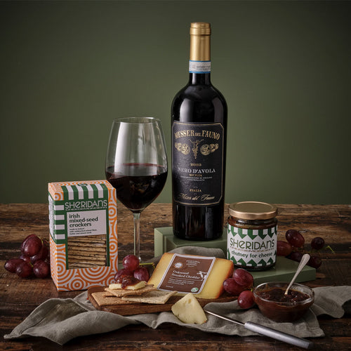 Wine bottle, glass, and assorted snacks on a wooden table with a green background