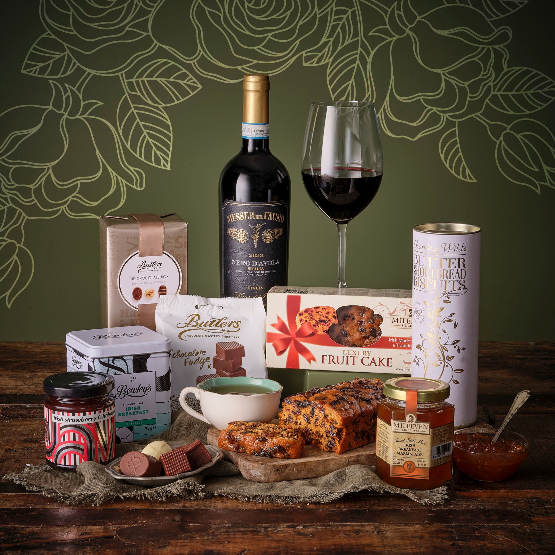 A Mother's Day Thank You Hamper featuring wine fruit loaf chocolates jam and a cup on a warm green background
