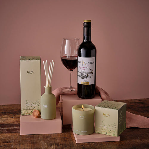 Wine bottle, candle, and diffuser on a wooden table with decorative elements.